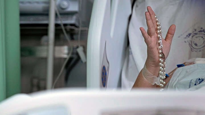 Un paciente de COVID-19 sostiene un rosario mientras los trabajadores de la salud del hospital de caridad portugués en Belem, estado de Pará, Brasil, cantan y oran por los pacientes con COVID-19 dentro de las salas y las áreas de la UCI. / Foto: AFP