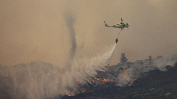 Sudáfrica-Un helicóptero con sistema Bambi Bucket, tripulado por el cuerpo de bomberos y unidades de rescate, intentan apagar un incendio forestal sobre el barrio residencial de Glencairn, el 22 de diciembre.