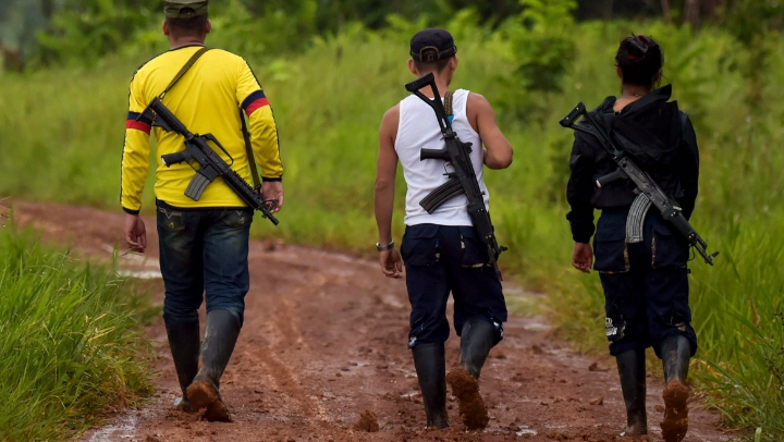 Niños reclutados por grupos armados caminan con fusil al hombro por una vía rural. 