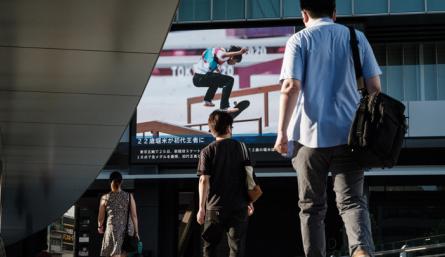 La gente camina frente a un tablero de anuncios eléctrico que muestra al japonés Yuto Horigome, el primer medallista de oro en la calle masculina de Skateboarding de los Juegos Olímpicos de Tokio 2020, en Tokio, este domingo. / Foto AFP