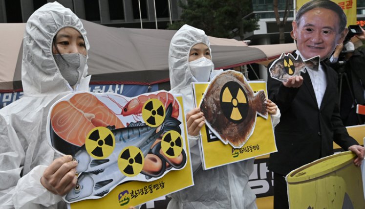 Activistas ambientales surcoreanos con ropa protectora y una máscara (R) del primer ministro de Japón, Yoshihide Suga, sostienen imágenes de peces con carteles de advertencia de radiactividad durante una protesta contra la decisión de Japón de liberar las aguas residuales de Fukushima, cerca de la embajada japonesa en Seúl. / Foto: AFP