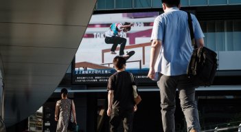 La gente camina frente a un tablero de anuncios eléctrico que muestra al japonés Yuto Horigome, el primer medallista de oro en la calle masculina de Skateboarding de los Juegos Olímpicos de Tokio 2020, en Tokio, este domingo. / Foto AFP